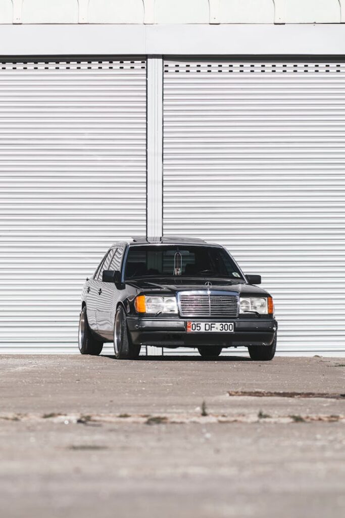 Elegant black Mercedes Benz car parked in front of a large garage with white shutters.